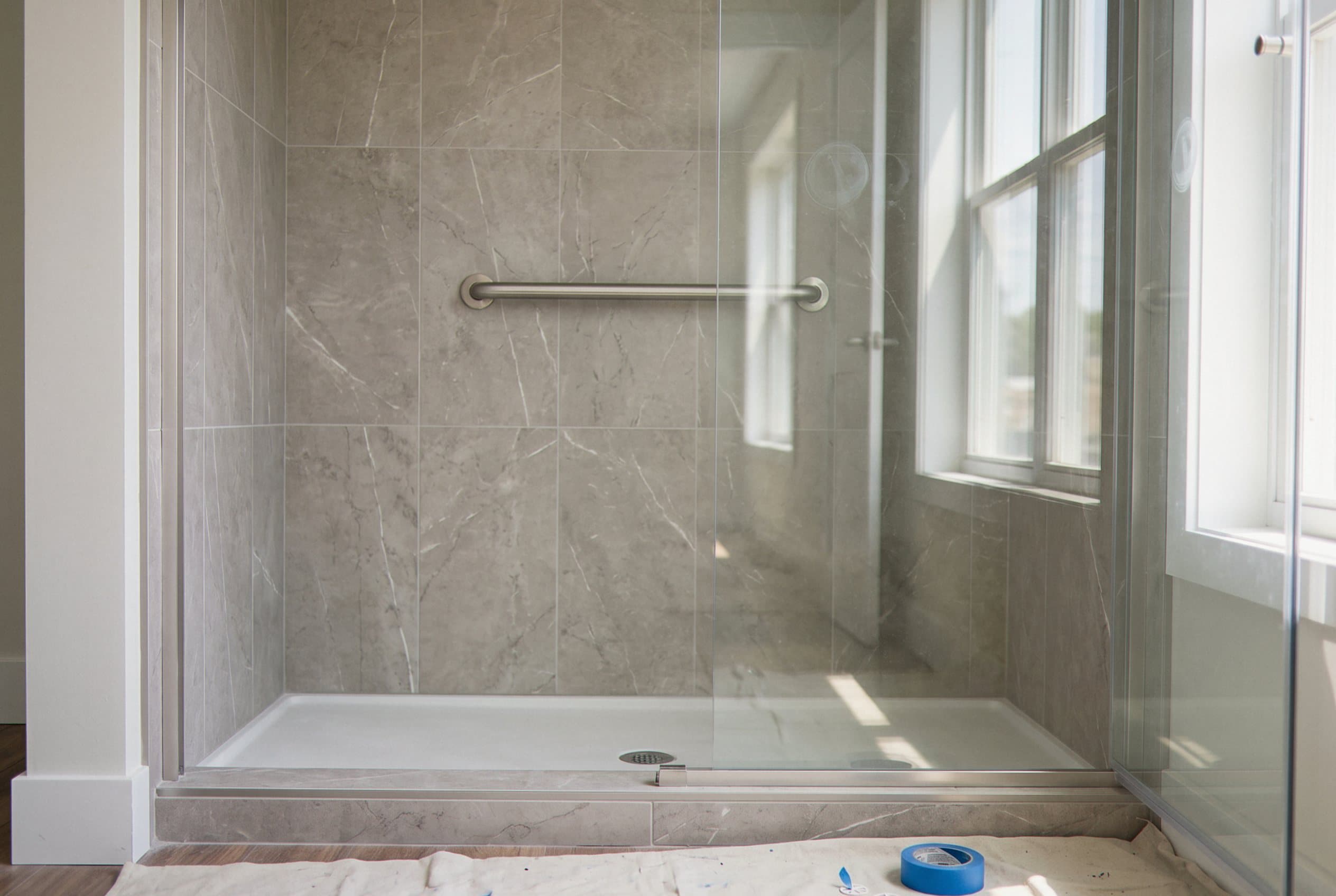 Converted walk-in shower with grey tile and grab bar